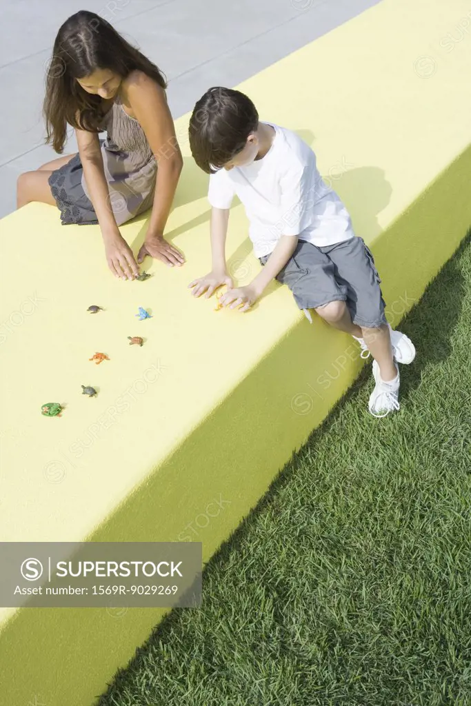 Mother and boy sitting outdoors, playing with plastic animal figurines, high angle view, full length