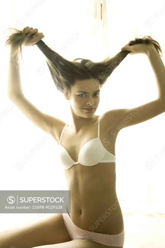 Young woman in bra holding up hair with both hands, smiling at camera
