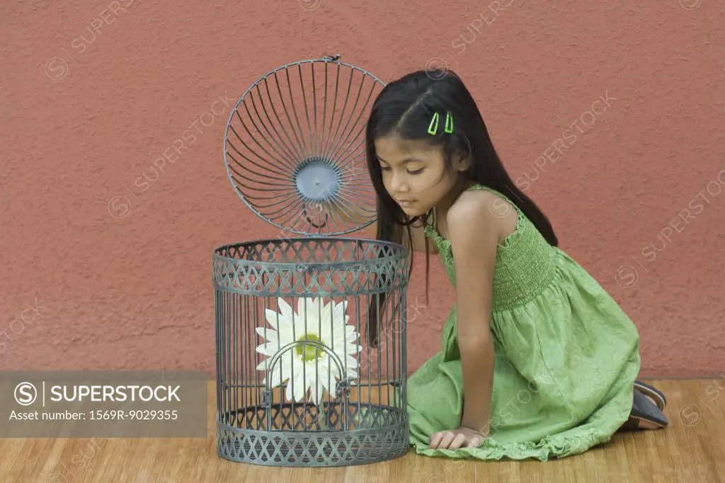 Girl opening up birdcage, looking at flower
