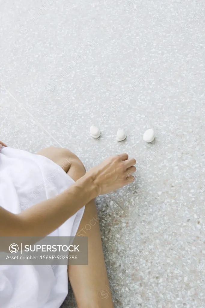 Woman kneeling on the ground arranging pebbles, cropped high angle view