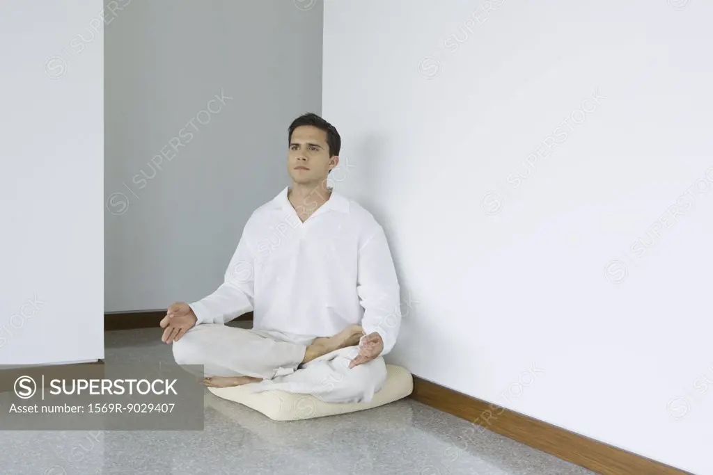 Man sitting in lotus position on cushion, looking away