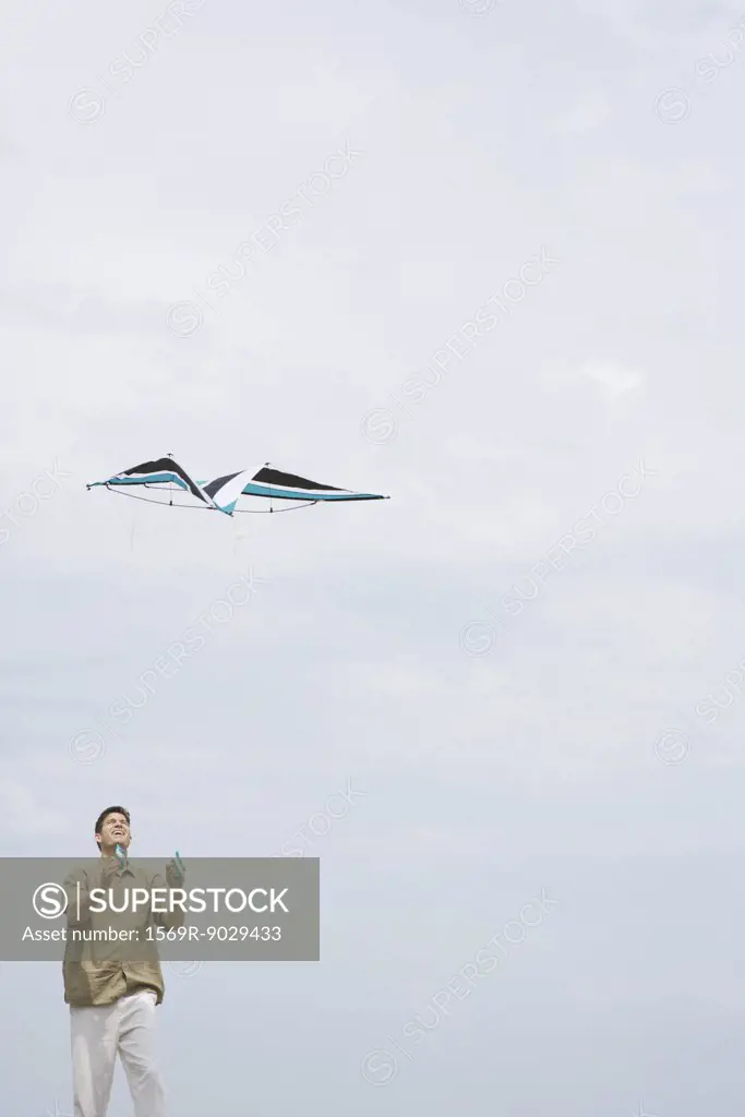 Man flying kite, looking up, three quarter length