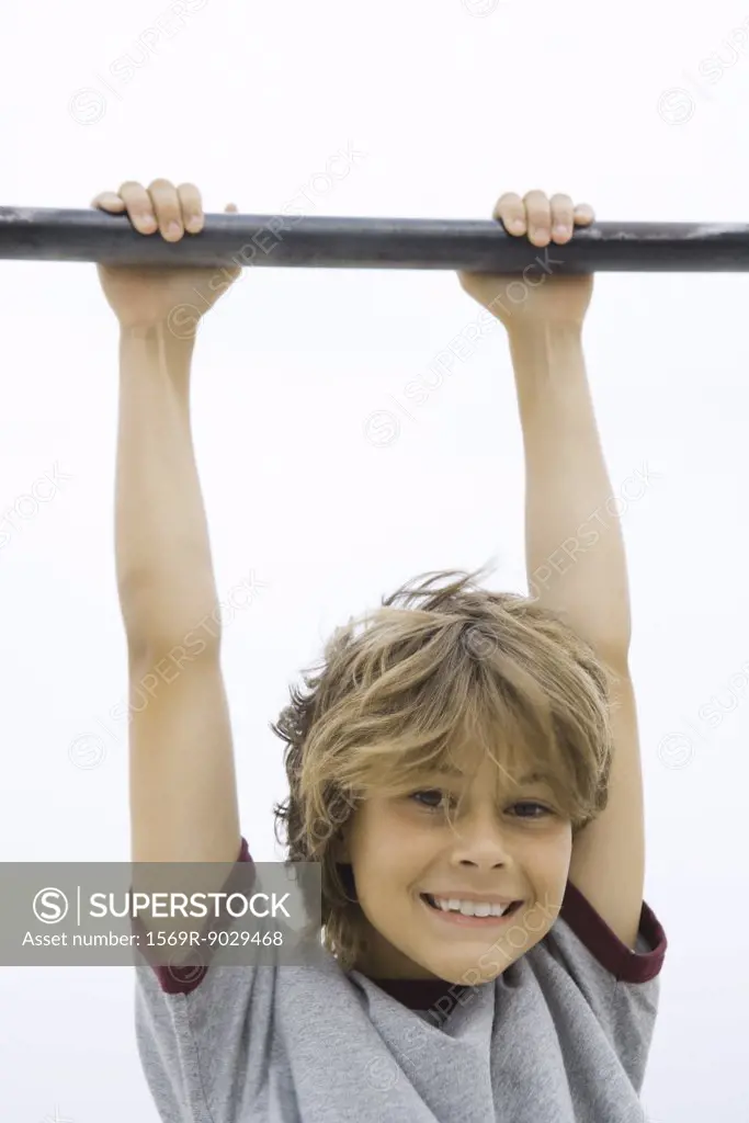 Boy hanging from metal bar, smiling at camera, portrait