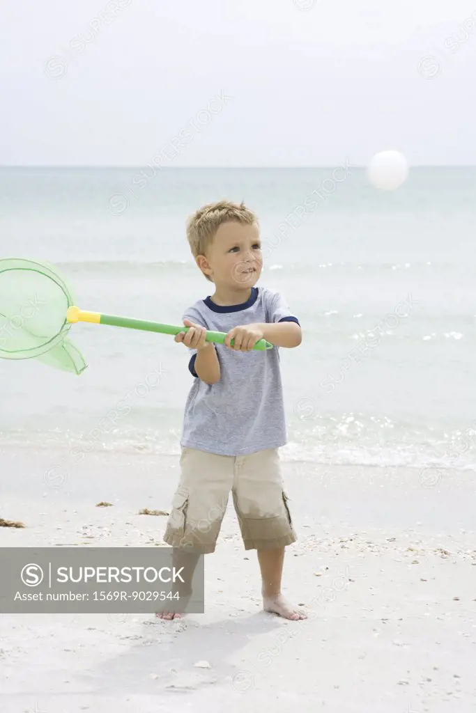 Young boy standing at the beach, holding up net to catch ball