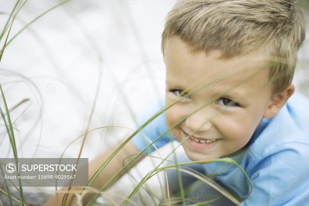 Young boy crouching in tall grass, smiling at camera