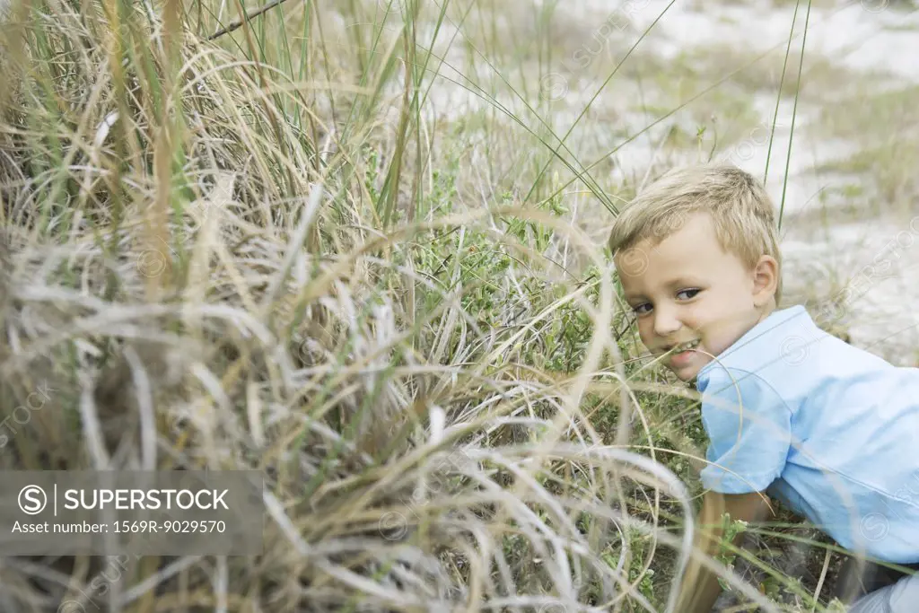 Young boy crouching in tall grass, looking away