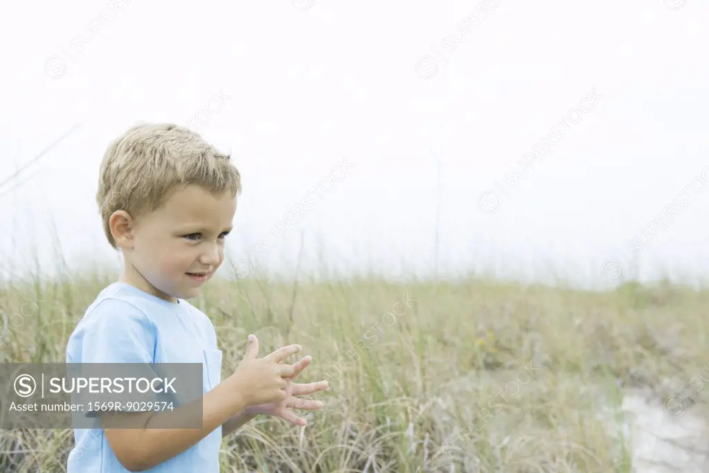Young boy standing in tall grass, looking away, side view