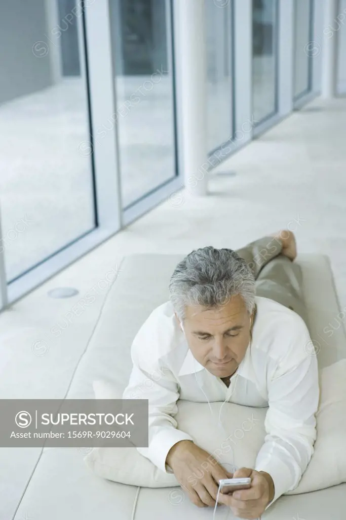 Mature man lying on chaise longue listening to mp3 player, high angle view