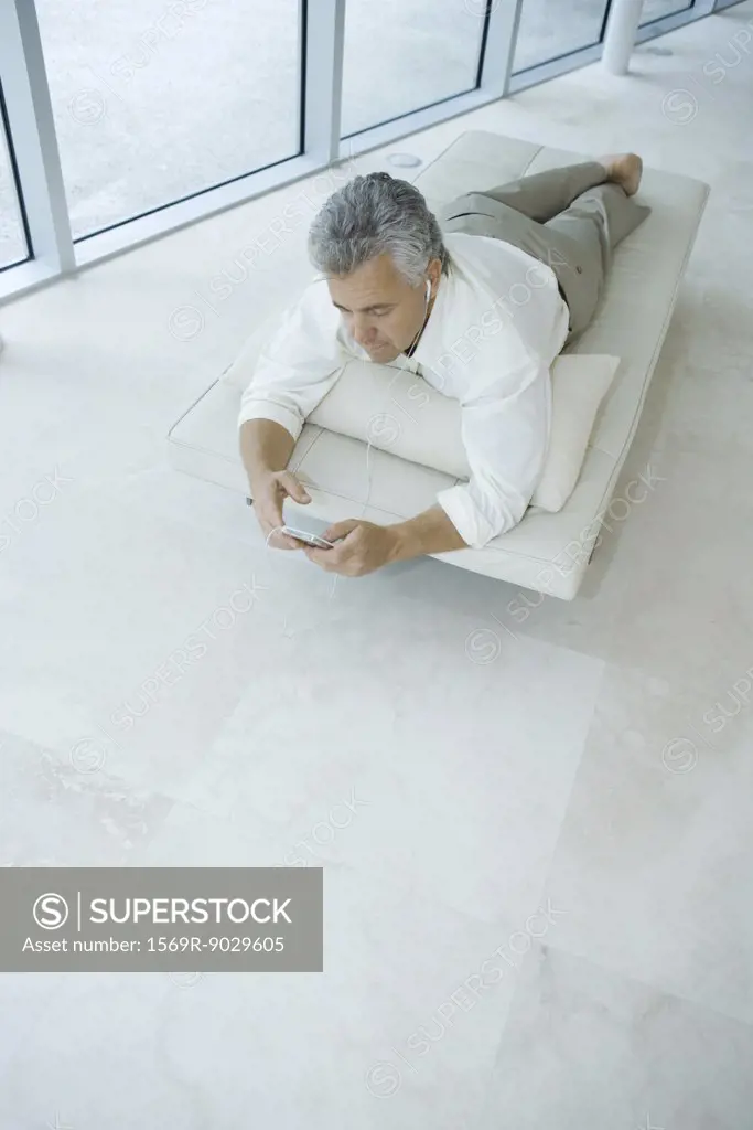 Mature man lying on chaise longue listening to mp3 player, high angle view