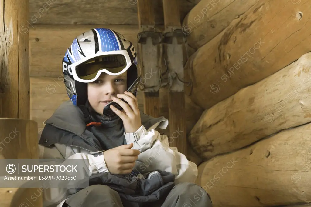Boy in ski gear sitting, using cell phone