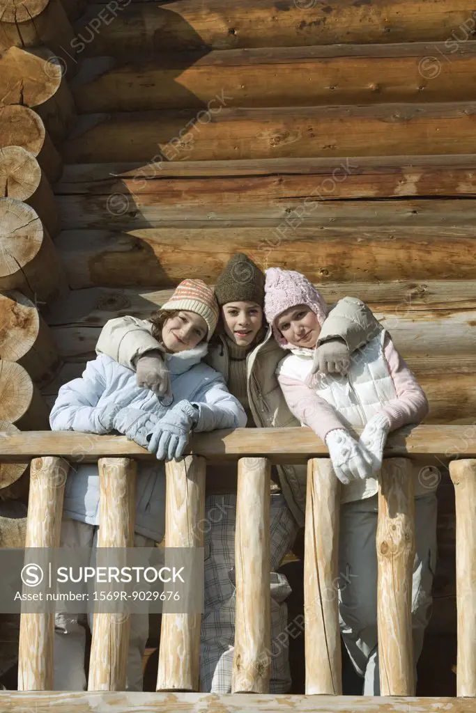 Three preteen or teen girls standing on deck of log cabin, smiling at camera