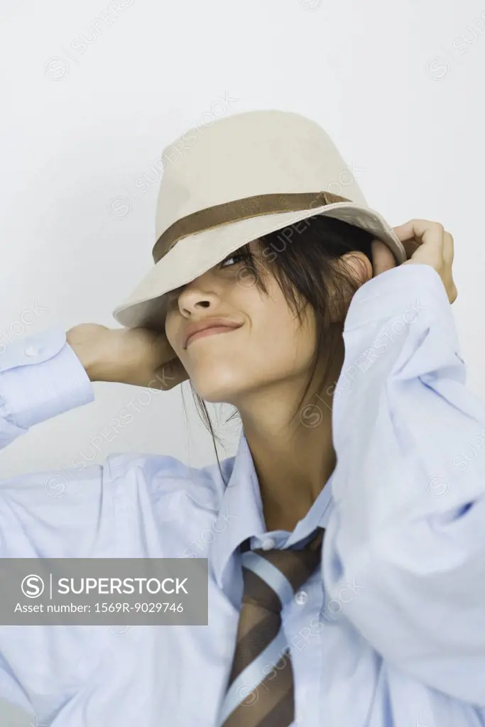 Teenage girl wearing tie, putting on hat, smiling at camera