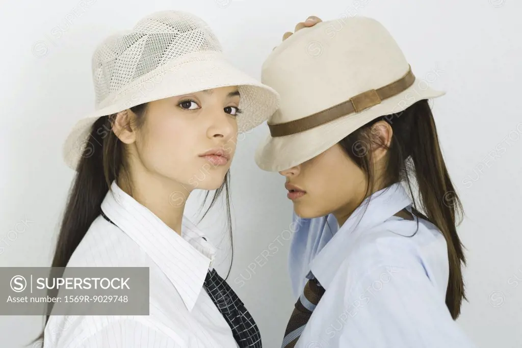 Two young female friends wearing hats, one looking at camera, the other's eyes covered