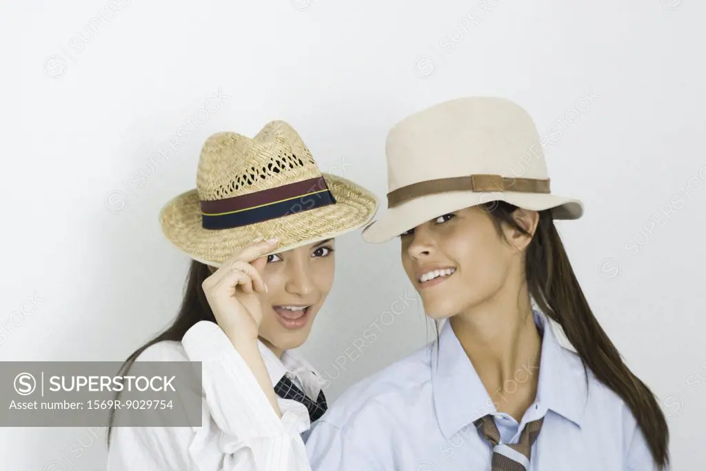 Two young female friends wearing hats and ties, both smiling at camera