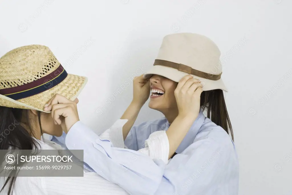 Two young friends pulling hats over each other's faces
