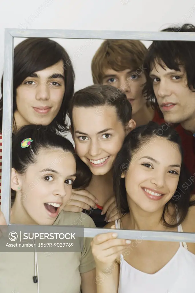 Young friends smiling at camera through picture frame, group portrait