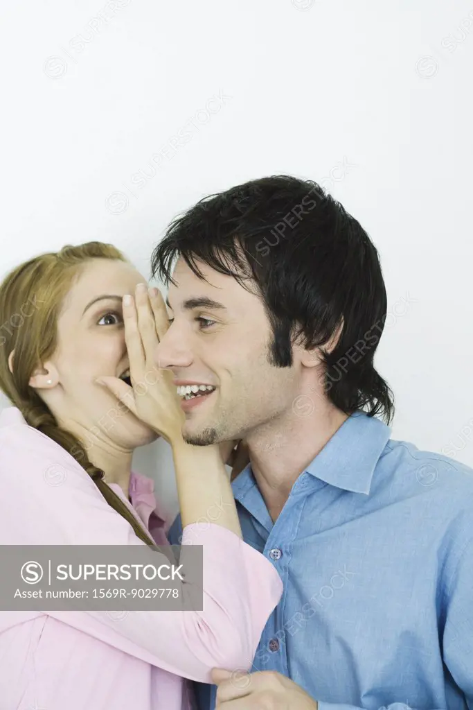 Young woman whispering in man's ear, close-up