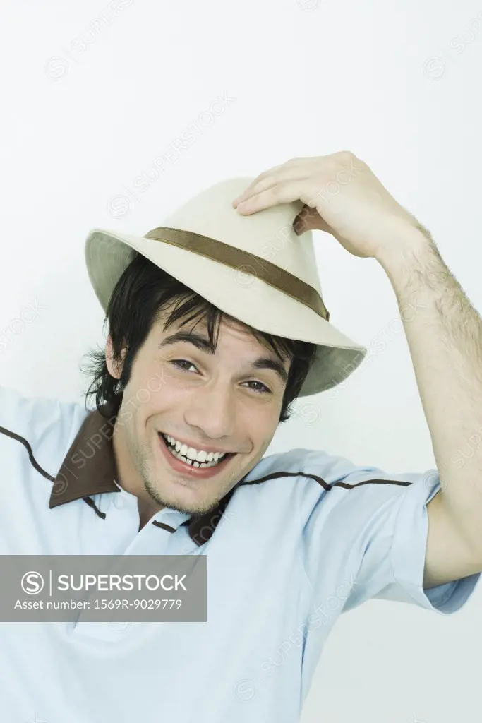 Young man putting hat on head, smiling at camera