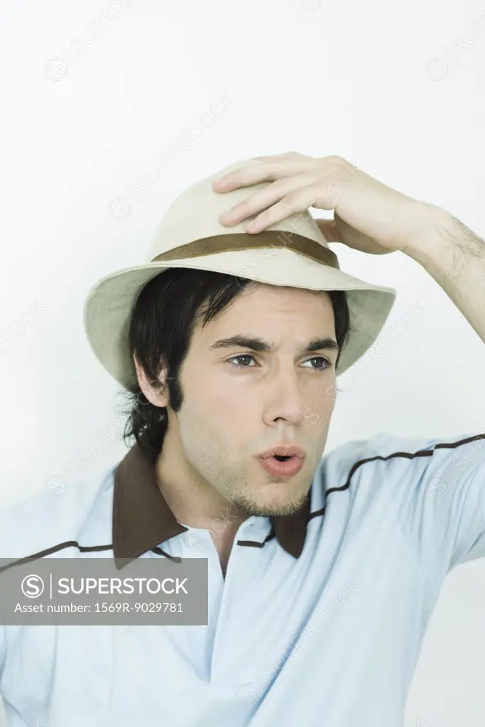 Man holding hat on head, looking away, puckering lips