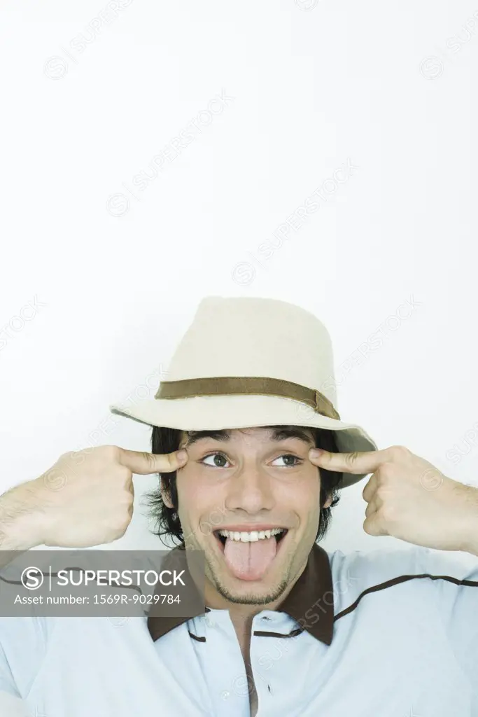 Young man wearing hat, sticking out tongue, pulling eyes to the side