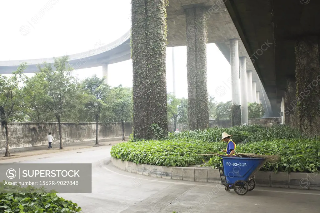 Public garden maintenance worker standing with cart under overpass