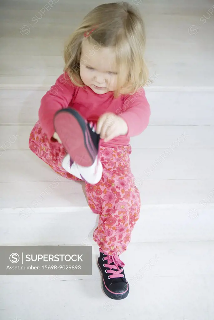 Blonde toddler girl putting on shoes, full length