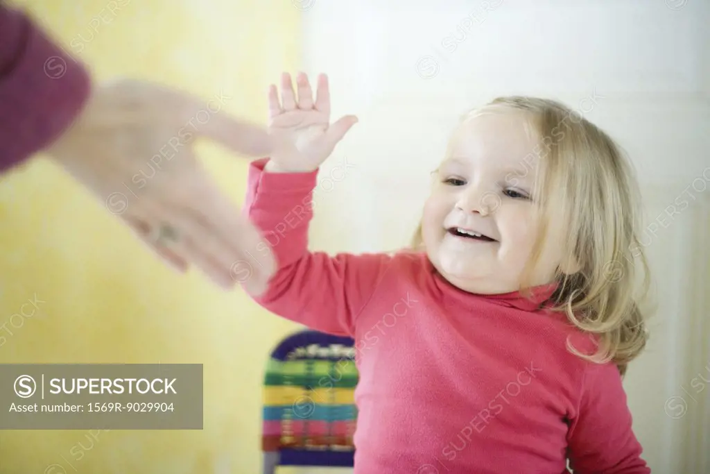 Blonde toddler girl giving adult high five