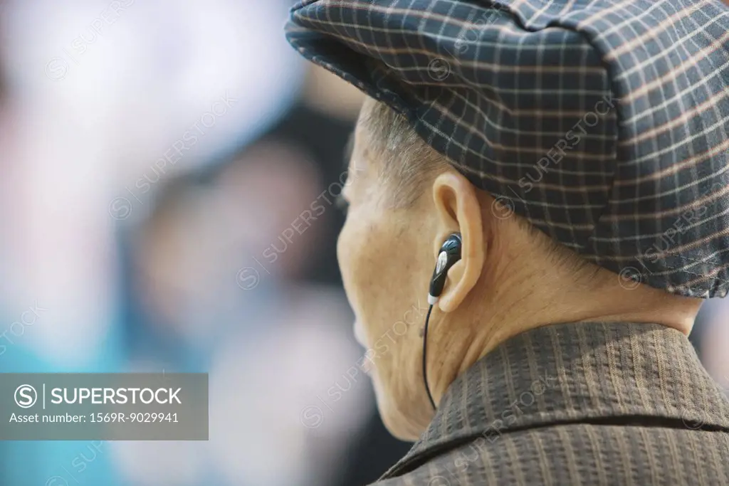 Senior man listening to earphones, rear view, head and shoulders