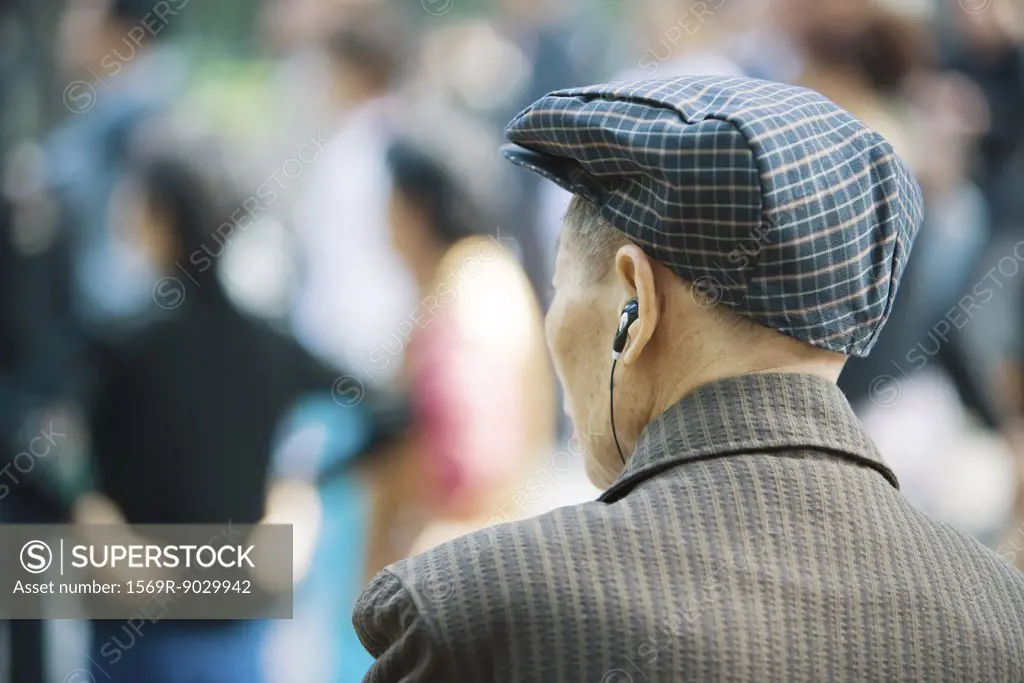 Senior man listening to earphones, rear view, head and shoulders