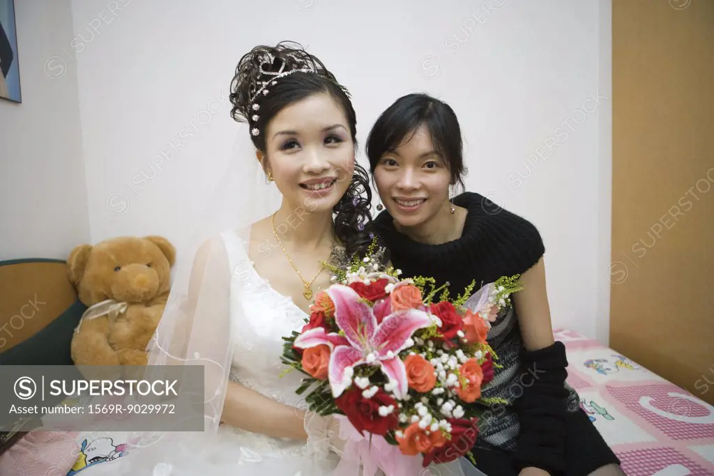 Bride sitting on bed with female friend, smiling, portrait