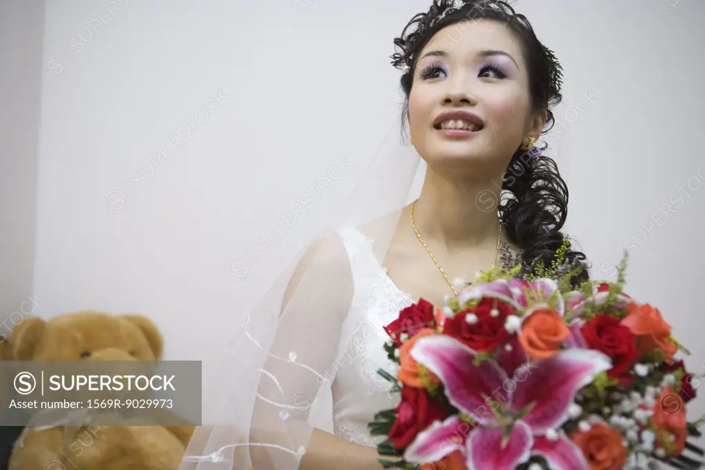 Bride holding bouquet, smiling, teddy bear in background