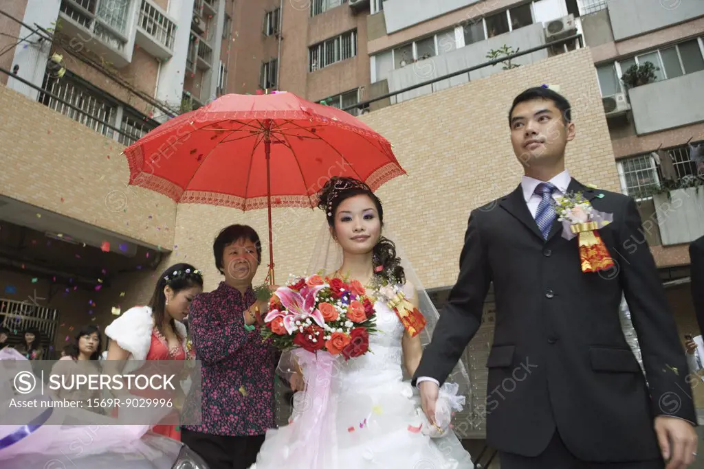 Chinese wedding, bride and groom leaving under confetti, bride covered by red parasol