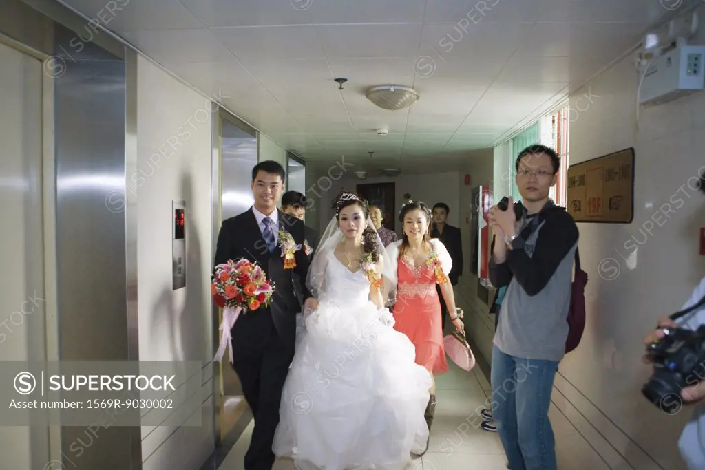 Bride and groom walking through hallway while photographers stand ready with cameras
