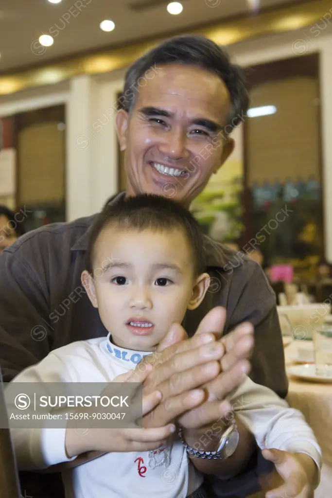 Man holding toddler on lap, clapping, smiling at camera