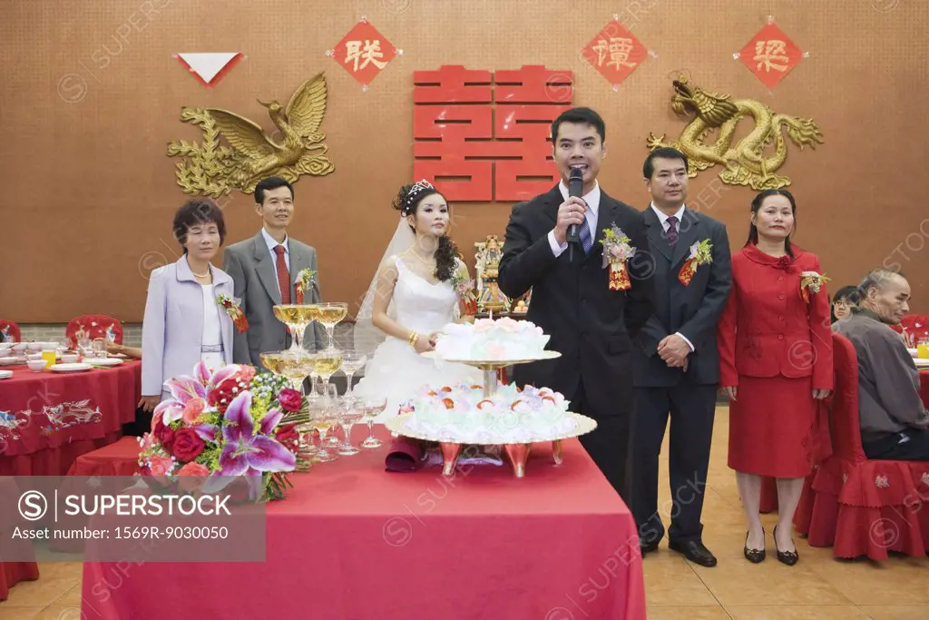 Groom standing in front of bride and parents, speaking into microphone