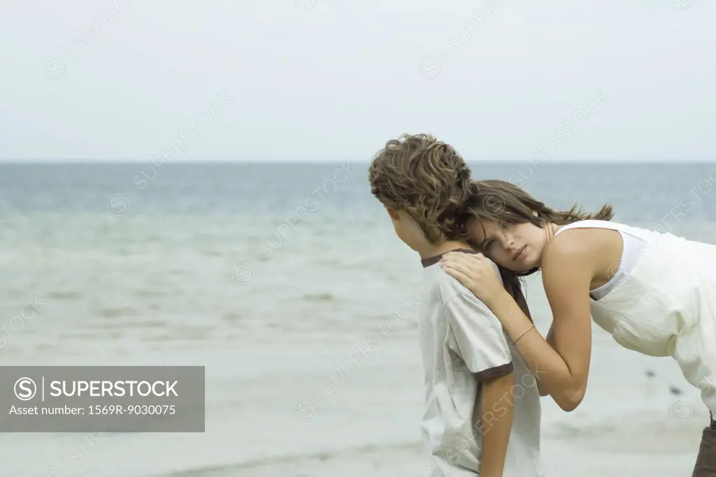 Teenage girl at the beach, leaning head against brother, looking at camera
