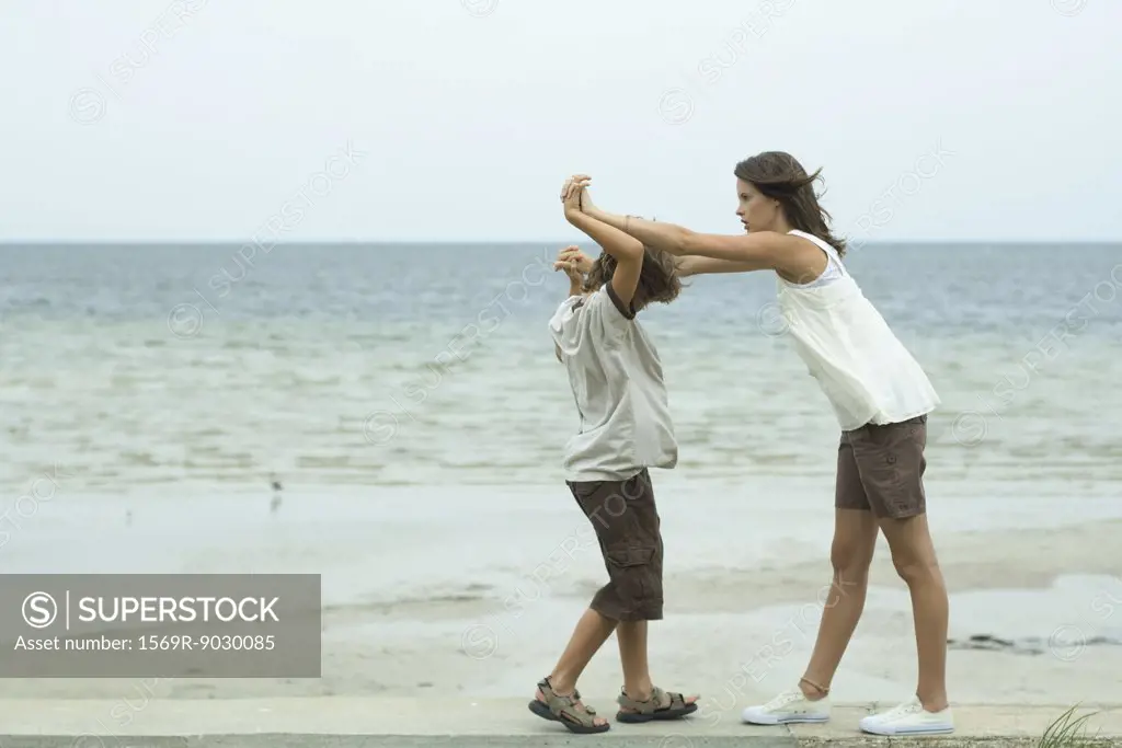 Brother and sister standing face to face at the beach with clasped hands
