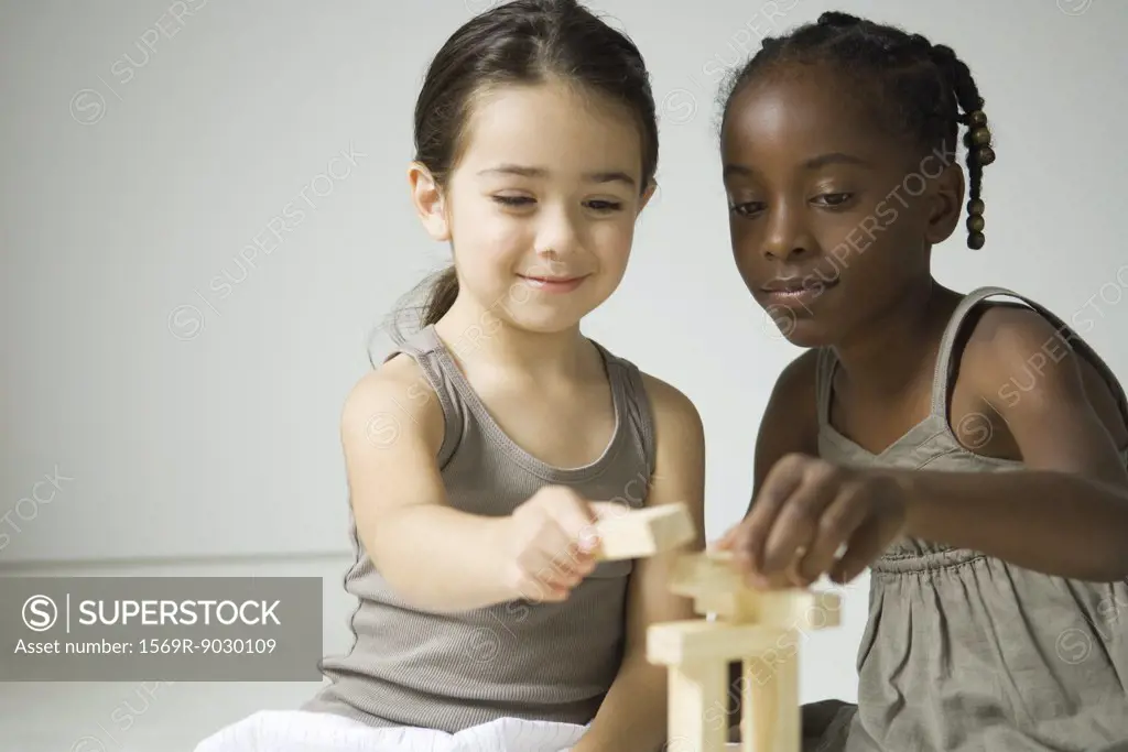 Two girls playing with blocks together, one smiling at camera