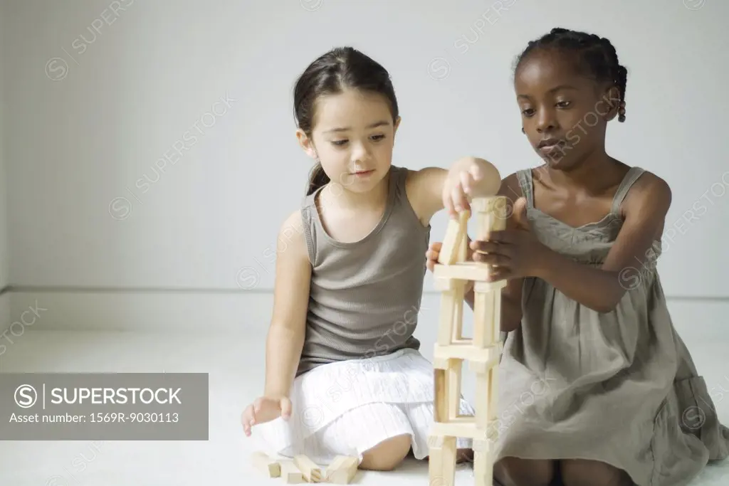 Two girls crouching, building tower with blocks together
