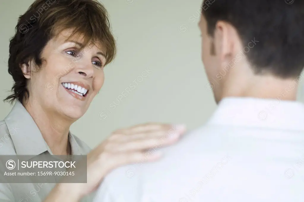 Woman smiling at man in foreground and placing her hand on his shoulder, cropped view