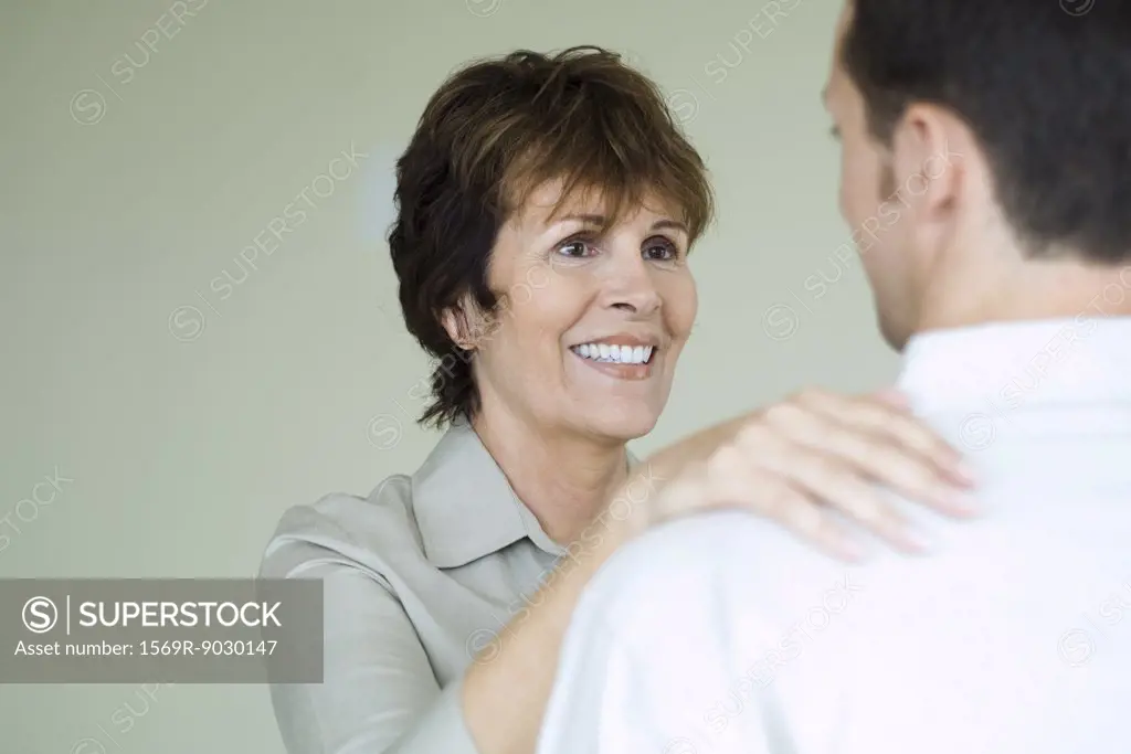 Senior woman standing in front of adult son with her hand on his shoulder, smiling