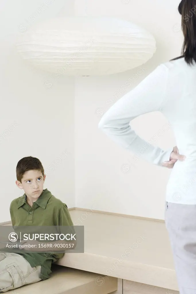 Boy holding  video game glaring at mother who watches him with hands on hips