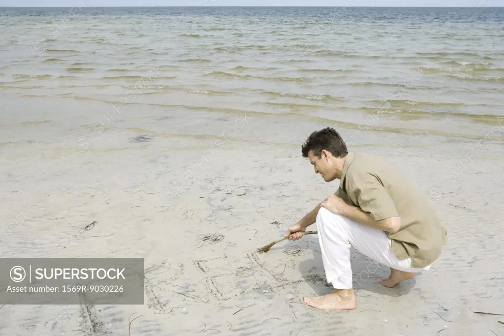 Barefoot man writing word "free" on beach with stick, full length
