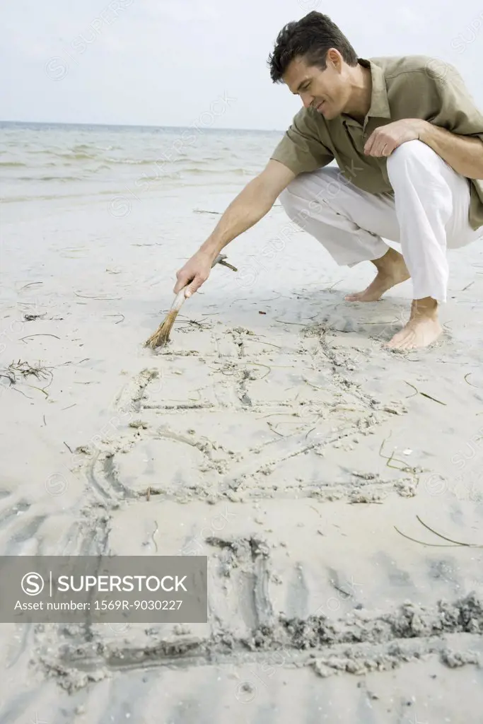 Barefoot man writing word "free" on beach with stick