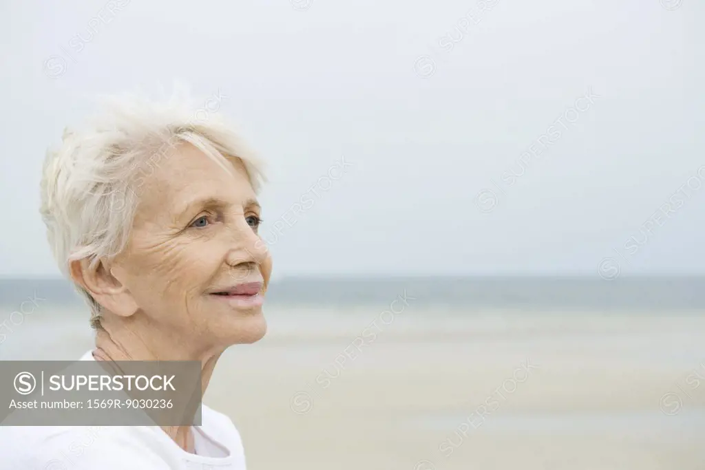 Senior woman smiling, looking away, beach in background