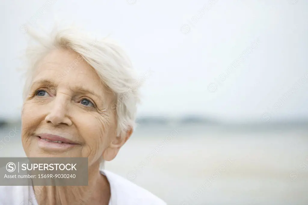Senior woman smiling, looking up, beach in background