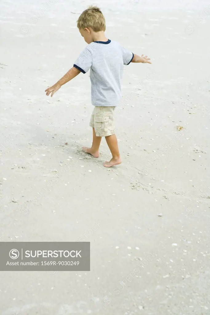 Little boy walking on beach with arms out, full length