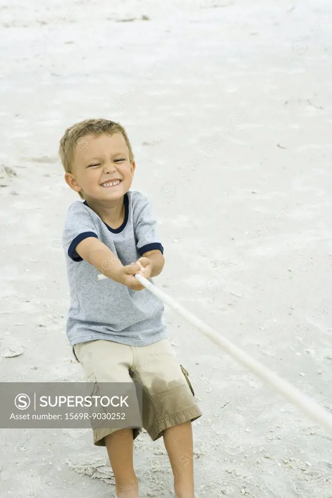 Little boy pulling on rope, making face, on beach
