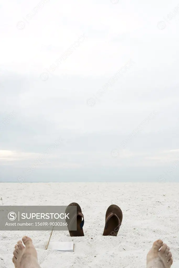Flipflops sticking out of sand, bare feet in foreground