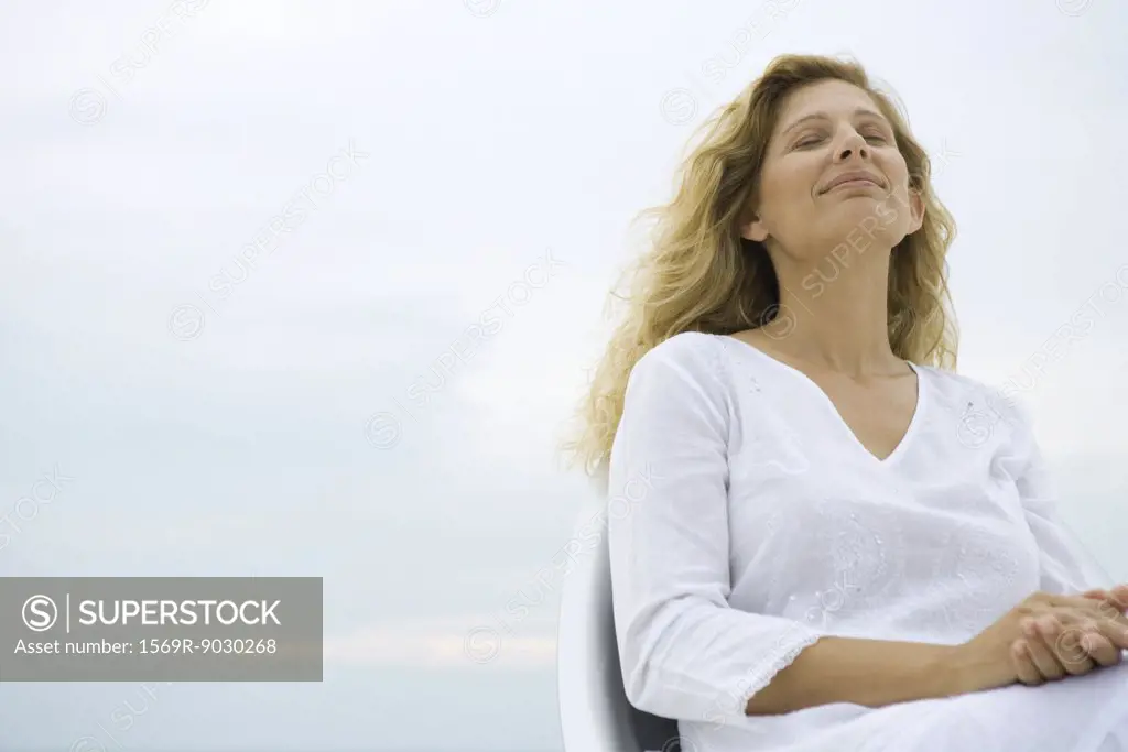 Woman sitting with eyes closed, smiling, sky in background, low angle view